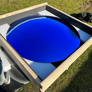 Puede incluir: Una gran superficie circular de color azul profundo y reflectante, encerrada en una caja de madera cuadrada. La caja est&aacute; forrada con espuma blanca para asegurar el objeto. Un taladro inal&aacute;mbrico est&aacute; colocado cerca de la esquina de la caja.