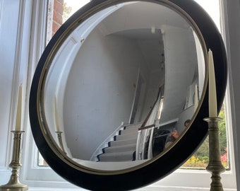 Pode incluir: Um espelho convexo redondo com uma moldura preta e uma moldura dourada. O espelho reflete uma escada e uma pessoa em pé em um corredor.