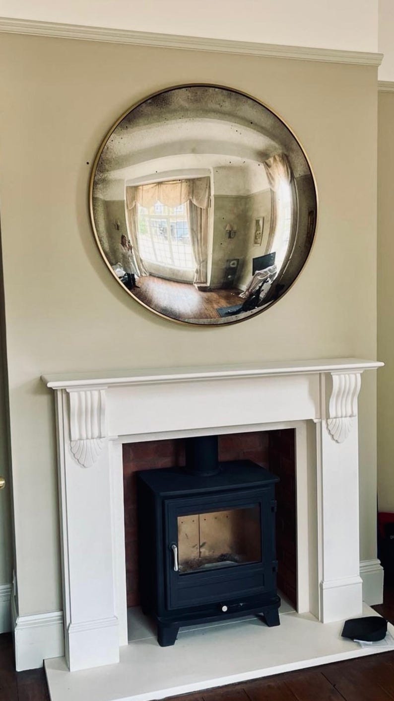 May include: A white fireplace with a black wood-burning stove. A large round convex mirror with a gold frame hangs above the fireplace.