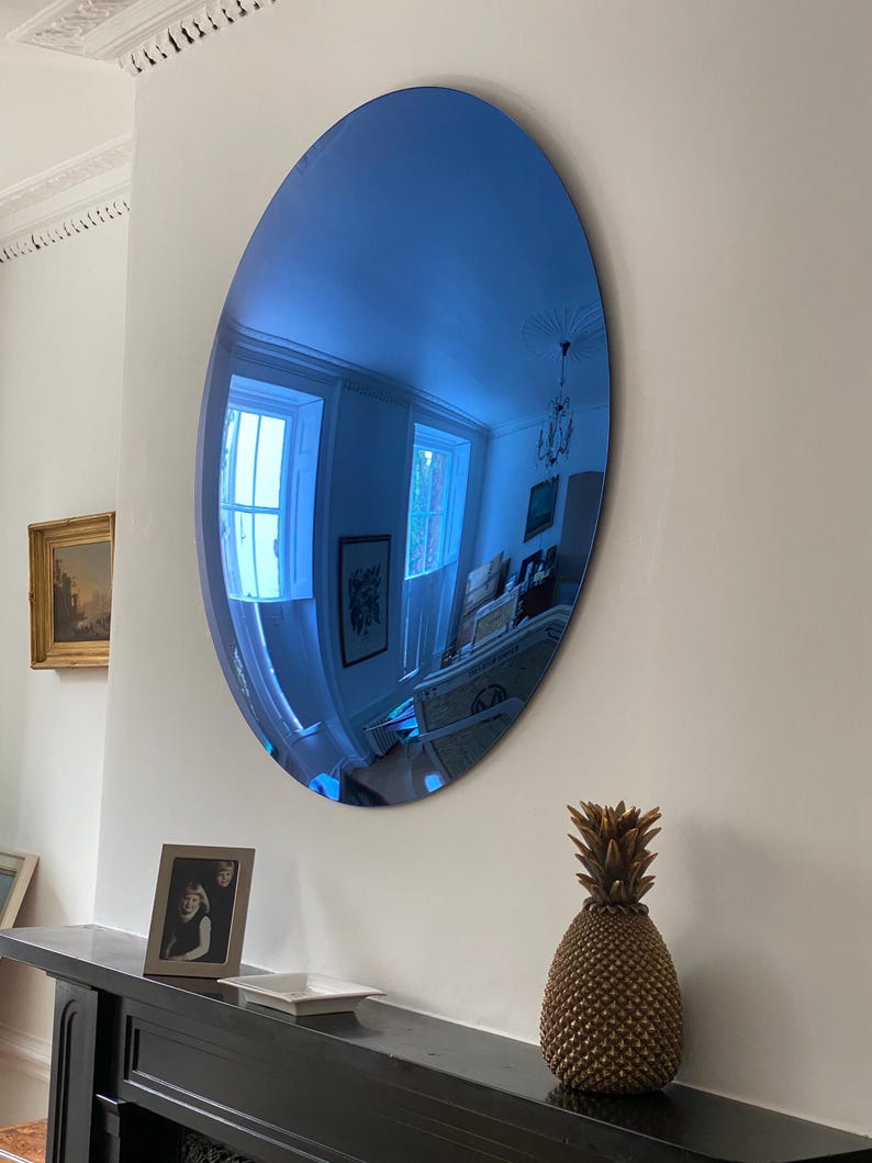 Puede incluir: Un gran espejo ovalado sin marco con una superficie reflectante de tono azulado. El espejo est&aacute; montado en una pared lisa y refleja la habitaci&oacute;n circundante, incluyendo ventanas, una l&aacute;mpara de techo y otros detalles arquitect&oacute;nicos.