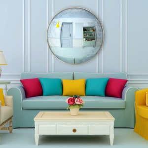 Pode incluir: Um interior de sala de estar com um sof&aacute; azul claro, duas poltronas, uma mesa de centro e um grande espelho redondo na parede. O sof&aacute; tem almofadas coloridas em tons de vermelho, amarelo, azul e turquesa. As poltronas s&atilde;o amarelas e bege. A mesa de centro &eacute; branca com uma gaveta. H&aacute; flores em um vaso sobre a mesa de centro.