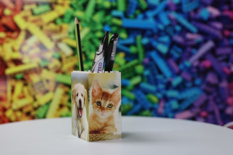 May include: A white pencil holder with a picture of a dog and a cat on the front. The holder is filled with a pencil and two pens.