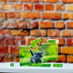 Op de afbeelding: Een witte plastic puzzel met een afbeelding van een kitten in groen gras. De puzzel is in de vorm van een kleine toren geassembleerd.