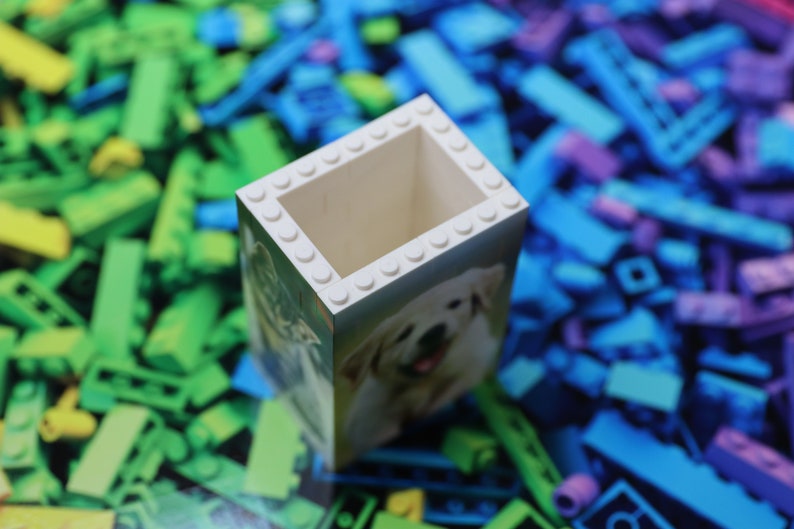 May include: White Lego brick pencil holder with a picture of a golden retriever dog on the front. The holder is surrounded by colorful Lego bricks.