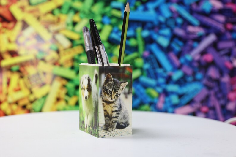 May include: A white ceramic pencil holder with a photo of a puppy and a kitten on the front. The holder is filled with pens and pencils.