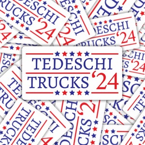 May include: A white sticker with red and blue text that reads "TEDESCHI TRUCKS '24". The sticker has five red stars on each side of the text.