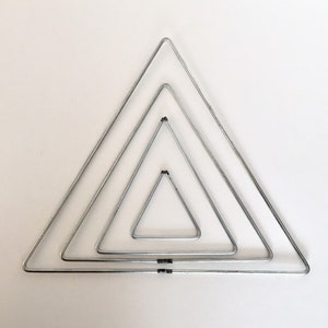 May include: Four silver metal triangles of different sizes, nested inside each other, forming a geometric pattern.