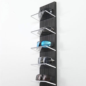 May include: A black wooden wall mounted rack with six clear acrylic shelves for storing sunglasses. The shelves are angled to display the sunglasses.