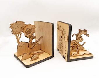 May include: A pair of light-colored wooden bookends featuring laser-cut designs of Calvin and Hobbes. One bookend depicts a character under a tree, while the other shows a character jumping, with the text Calvin and Hobbes engraved on the side.