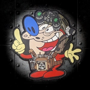 Könnte beinhalten: Eine Comicfigur mit blauen Augen und einem roten Overall trägt einen schwarzen und grünen Helm mit dem Text "FREEDOM FIGHTER" darauf. Die Figur zeigt den Daumen nach oben und hat ein breites Lächeln.