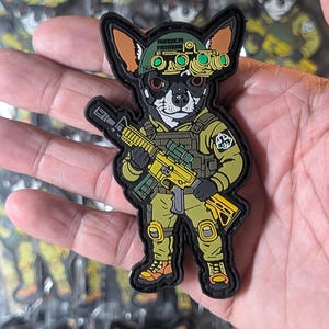 May include: A patch featuring a chihuahua in military gear, holding a yellow rifle. The dog wears a helmet with the text "Freedom Fighters" and night vision goggles. The patch is olive green, black, and yellow.