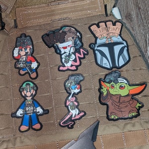 Könnte beinhalten: Sechs gestickte Aufnäher mit verschiedenen Comicfiguren. Die Aufnäher sind alle in verschiedenen Farben und mit verschiedenen Designs. Die Aufnäher sind alle auf einem braunen Stoffhintergrund befestigt.