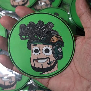May include: A green circular patch featuring a cartoon illustration of a person wearing night vision goggles and a headset. The patch has the words "FREEDOM FIGHTERS" printed on it. The image is of several patches.