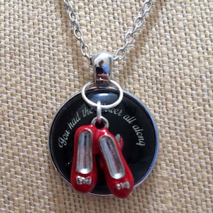 Puede incluir: Un collar de plata con un colgante negro que presenta un par de zapatillas rojas de rubí y el texto "You had the power all along".