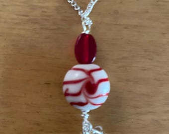May include: A silver chain necklace with a white and red glass bead and a red glass bead pendant.
