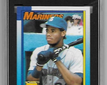 May include: A 1990 Topps baseball card featuring Ken Griffey Jr. in his Seattle Mariners uniform. The card is in a protective case with a grade of 9.