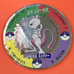 May include: A silver Pokemon trading card featuring a silver and pink Mewtwo Pokemon character. The card has a green, yellow, red, and purple background with the text "Pocket Monsters" and "Pokemon Trading Card Game" in Japanese. The card also has the text "Mewtwo" and "No. 87" in Japanese.
