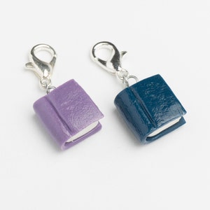 May include: Two small book charms with silver clasps. The book on the left is purple and the book on the right is blue.