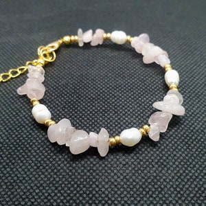 May include: A delicate bracelet featuring a mix of pink rose quartz and white pearl beads, connected by gold-toned spacers. The bracelet has a lobster clasp closure.