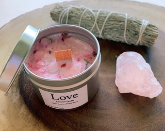 May include: A silver tin candle with a pink wax base and rose quartz crystals. The candle is labeled "Love Crystal Candle Rose Quartz | Dried Roses Soy Wax Candle".