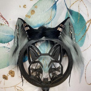 Könnte beinhalten: Ein schwarzes Katzenohren-Stirnband mit grauem und schwarzem Kunstfell. Die Ohren haben silberne Akzente und Sternanhänger. Das Stirnband zeigt ein schwarzes Katzengesicht-Design in der Mitte.
