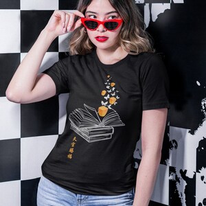 以下が含まれることがあります： 蝶が本から飛び出しているグラフィックがプリントされた黒いTシャツ。Tシャツには「大有智慧」という文字がプリントされています。