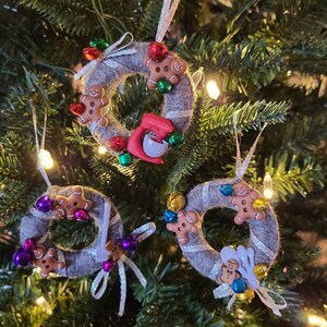Könnte beinhalten: Drei graue Filz-Weihnachtsornamente in Form von Kränzen, verziert mit Lebkuchenmännern, Glocken und anderen festlichen Details.
