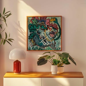 Puede incluir: Una obra de arte enmarcada con una vibrante ilustración de estilo grafiti. La obra presenta una criatura verde y azul con una corona, rodeada de formas abstractas y texto garabateado. El marco es de color marrón cálido.