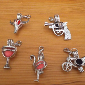 May include: Six silver charm pendants with different designs. The charms are in the shape of a bull's head, a gun, a wine glass, a flamingo, and a motorcycle. The charms are all silver and have a red or black enamel finish.
