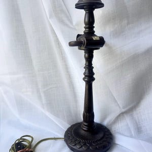 May include: A dark brown, vintage-style table lamp with a decorative base and a slender, ornate stem. The lamp has a small, round top and a cord with a plug. The base is approximately 6 inches in diameter.