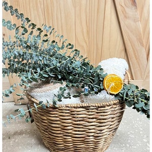 May include: A woven wicker basket filled with white towels and a dried orange slice, decorated with eucalyptus sprigs.