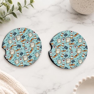 May include: Two round car coasters with a light blue background and a pattern of medical supplies. The pattern includes stethoscopes, pill bottles, bandages, and clipboards. The coasters have a small notch for easy removal.