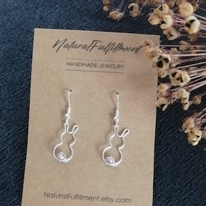 Könnte beinhalten: Ein Paar silberne Ohrringe in Hasenform mit einer kleinen rosa Perle an jedem Ohrring. Die Ohrringe werden auf einer braunen Karte mit dem Text "Natural Fulfillment Handmade Jewelry" und "NaturalFulfillment.etsy.com" präsentiert.