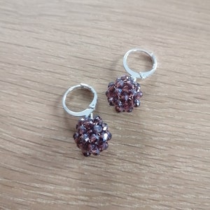Könnte beinhalten: Ein Paar silberne Creolen mit einem baumelnden braunen Kristallkugelschmuck.