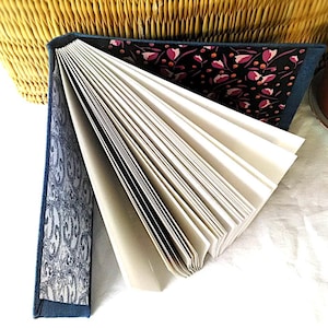 May include: An open journal with a blue denim cover and white pages. The inside cover features a black background with a floral pattern in pink and orange. The other inside cover has a white and blue paisley design.
