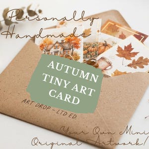 May include: A brown kraft paper envelope containing several small art cards featuring autumn-themed illustrations of a house, pumpkins, and fall leaves. The envelope is printed with the text "ART DROP - LTD ED." and a green overlay reads "AUTUMN TINY ART CARD."