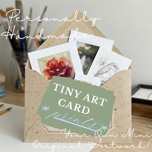 May include: A tan speckled paper envelope containing several small art cards. One card features a red flower, another a landscape, and a third a bird sketch. A green rectangular overlay displays the white text TINY ART CARD prints.