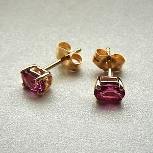 Puede incluir: Un par de pendientes de oro con piedras preciosas rosas. Los pendientes tienen un diseño simple de botón.