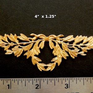 K&ouml;nnte beinhalten: Goldene Metall-Dekorverzierung mit einem Blattdesign und einer Schleife in der Mitte. Die Verzierung misst 10,16 cm x 3,17 cm.