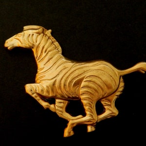 May include: A gold-colored metal zebra figurine, running with its head turned to the side. The zebra is detailed with stripes and has a textured surface.