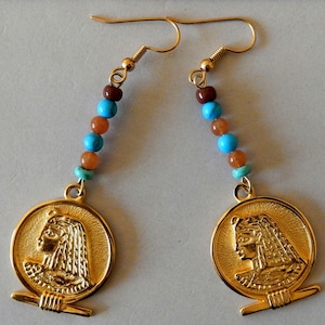 May include: Gold earrings with turquoise and brown beads and a gold pendant featuring a profile of an Egyptian queen.