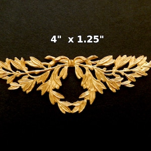 K&ouml;nnte beinhalten: Goldene Metall-Dekorverzierung mit Blatt- und Schleifendesign. Sie misst 10,16 cm x 3,17 cm.