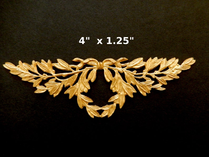 K&ouml;nnte beinhalten: Goldene Metall-Dekorverzierung mit Blatt- und Schleifendesign. Sie misst 10,16 cm x 3,17 cm.