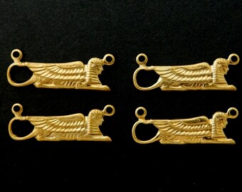 May include: Four gold-colored sphinx pendants, each with a detailed winged design and a loop for attachment. The pendants are arranged on a black background, showcasing their intricate craftsmanship and historical theme.