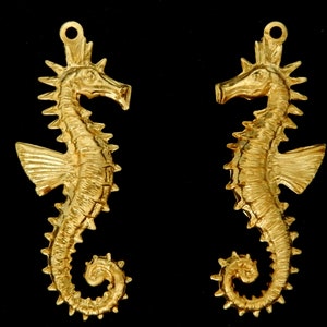 May include: Two gold-colored seahorse charms with detailed sculpting. The seahorses have a textured surface and are facing opposite directions.