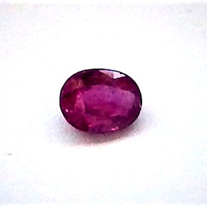 May include: A vibrant pink oval-shaped gemstone, likely a ruby, set against a white background.
