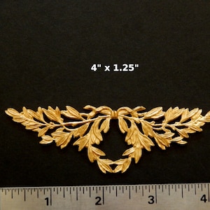 K&ouml;nnte beinhalten: Goldene Metall-Dekorverzierung mit einem Blattdesign und einer Schleife in der Mitte. Die Verzierung misst 10,16 cm x 3,18 cm.