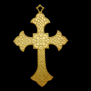 May include: A gold-colored metal cross with intricate designs. The cross has a rounded top and a pointed bottom.