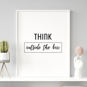 May include: A framed white print with the words "THINK outside the box" in black. A small cactus in a white and gray pot on a gold stand and a white hand sculpture holding a ball of twine are on a white shelf.