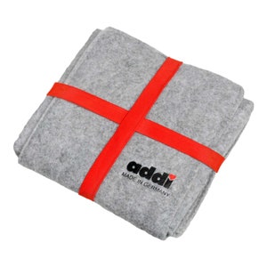 Könnte beinhalten: Eine graue Filz-Aufbewahrungstasche mit roten Bändern und dem Text "addi MADE IN GERMANY" mit einem roten Herzen.